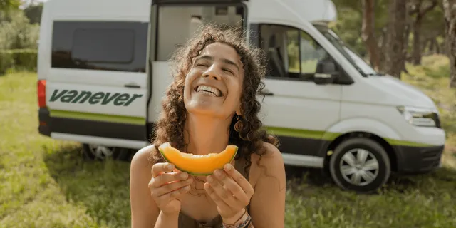 Frau lacht vor VW Grand California Campervan