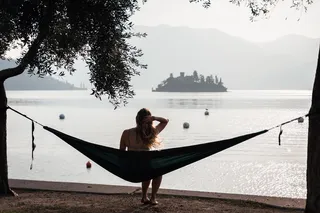 A woman sits on the shores of Lake Maggiore in a hammock and looks at an island.