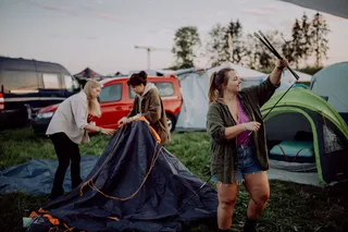 Three women at the tent building on a festival grounds. Everything you need for the Festival Camping can be found at our Festival Packliste.