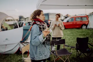 A woman stands with a table tennis ball on a festival grounds, around her you can see tents, camping chairs and another woman in the background. Our Festival Packlist can be found here.