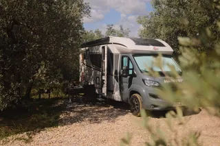 A camper is parked by the trees