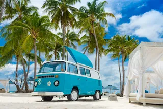Blue VW Bulli on beach with palms and surfboards