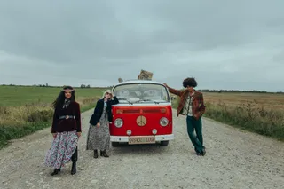Three hippies with VW Bulli and Peace sign on field