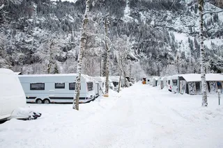A snowy campsite with some vans in front of a mountain scenery.